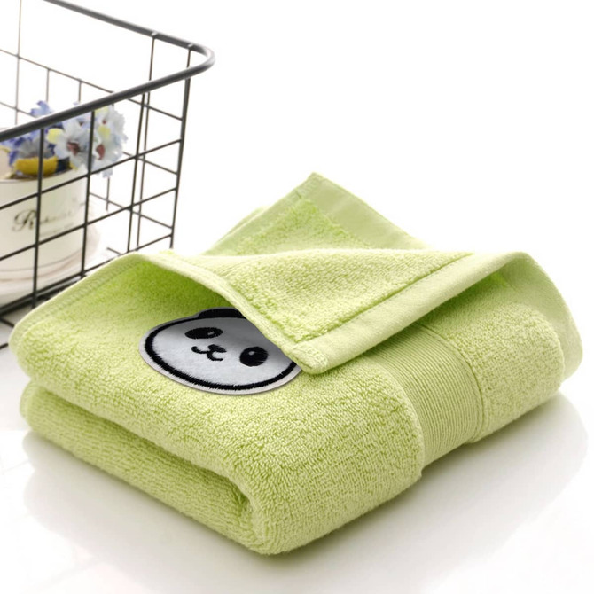 A folded green cotton hand towel featuring a panda design on the front. A wire basket is in the background.