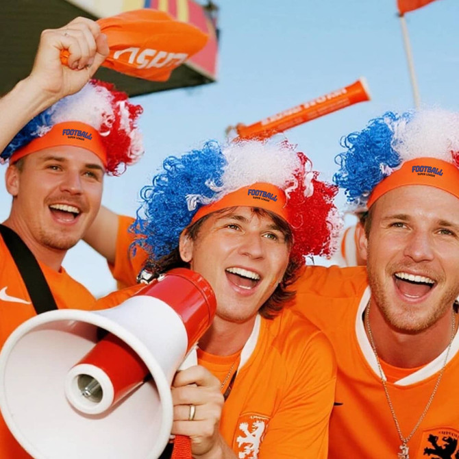 Three fans wearing bright orange jerseys, red, white, and blue wigs, cheering together at a sporting event with a megaphone.