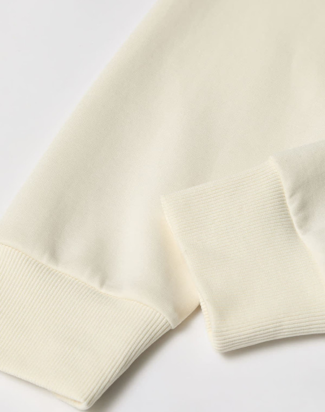 A crew neck sweater in a creamy off-white colour, featuring ribbed cuffs and a smooth fabric texture.