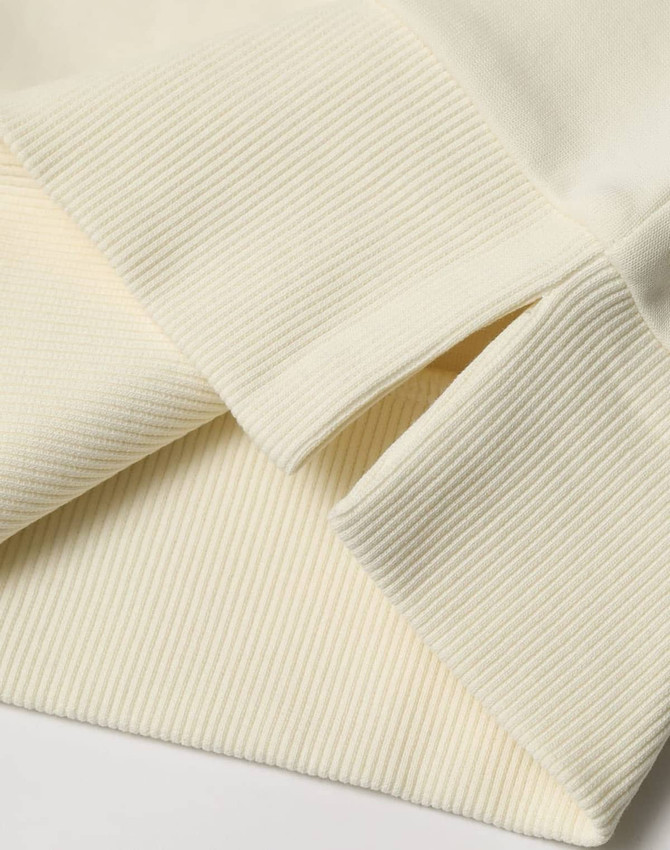 A close-up of a cream-coloured unisex crew neck sweater, featuring ribbed cuffs and hem. It has a logo.