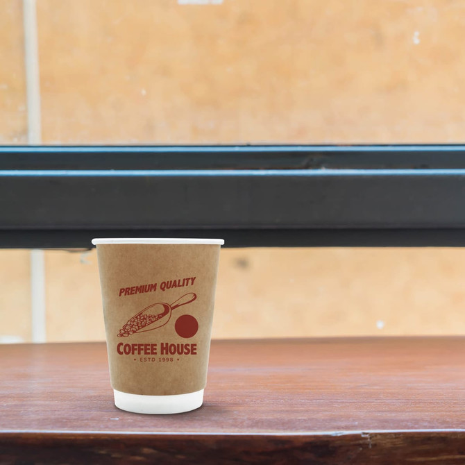 A kraft paper cup with a double wall design, featuring a red logo and sitting on a wooden surface.