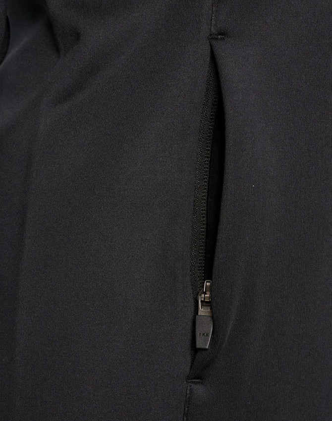 A close-up of a black softshell jacket featuring a zippered pocket. The fabric appears smooth and durable.