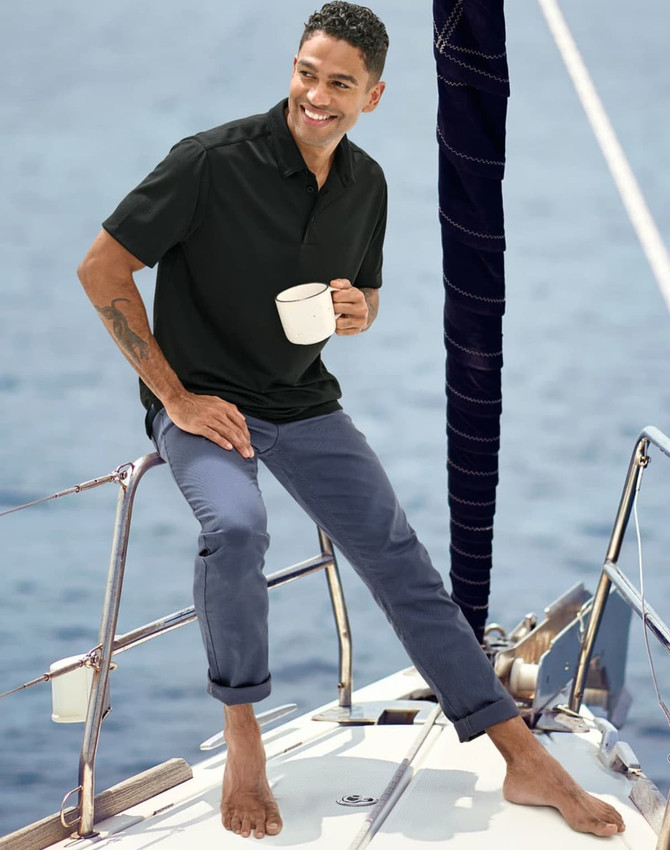 Men's flexi chino pants in navy, modelled by a man on a boat, wearing a black polo and holding a cup.