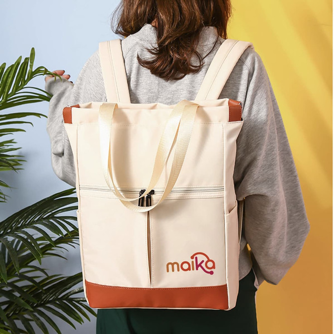 A beige convertible nylon backpack with brown accents and a logo, worn on a person’s back against a colourful background.