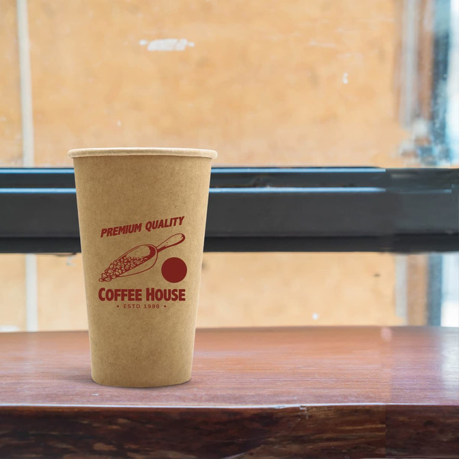 A kraft paper cup in brown, featuring a logo and design, placed on a wooden surface near a window.