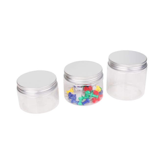 Three clear round containers with aluminium lids, containing colourful push pins in the middle one.