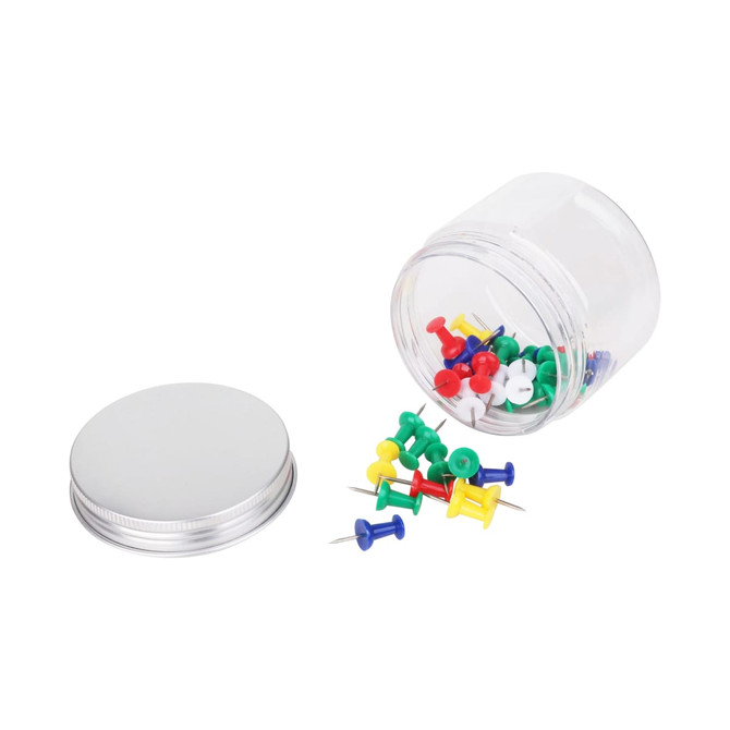A clear round container with an aluminium lid, containing assorted coloured push pins scattered around.