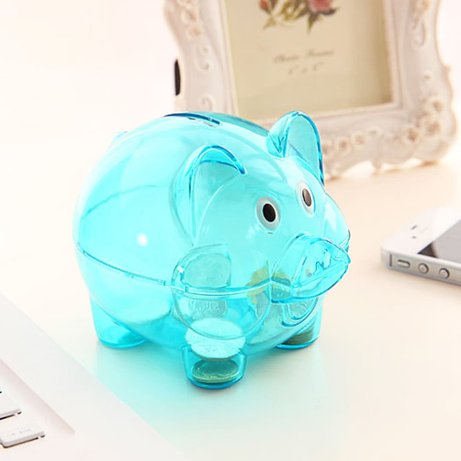 A transparent blue piggy coin bank with cartoonish features, placed on a desk alongside a phone and laptop.