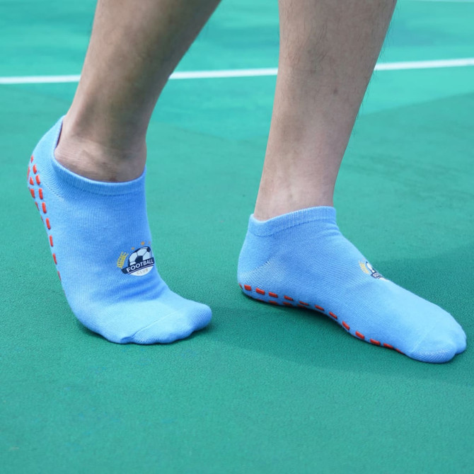 Low cut blue gripper socks featuring a logo and red silicone grips on the sole, displayed on a person's feet. Low cut blue gripper socks featuring a logo and red silicone grips on the sole, displayed on a person's feet.