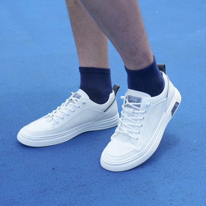 A pair of white shoes paired with navy crew socks on a blue surface, featuring a branding logo on the socks.