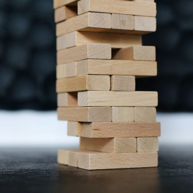 A wooden block tower made of light-coloured timber blocks, stacked in a stable formation against a blurred background.