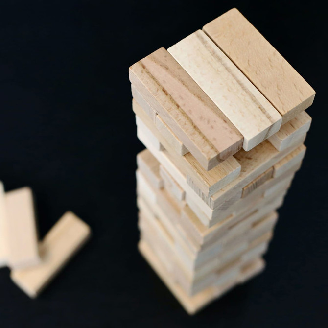 A wooden block tower stacked vertically with light and natural wood tones, alongside scattered blocks on a dark surface.