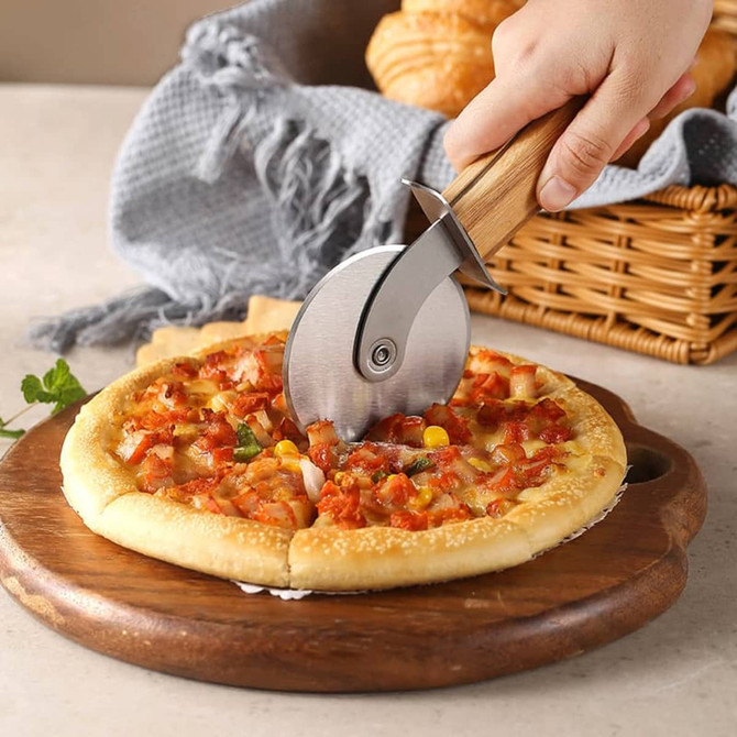 A pizza cutter wheel with a hand-carved wooden handle, slicing through a pizza on a wooden board.