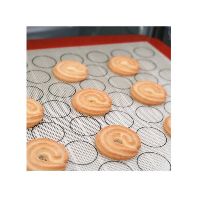 A silicone baking mat with a red border and circular markings, featuring freshly piped pastry swirls.