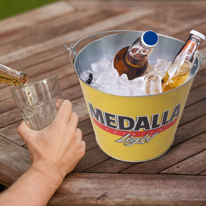A yellow ice bucket with a handle holds several bottles surrounded by ice, alongside a glass being filled.