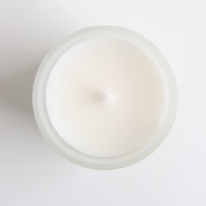 A white glass candle in a frosted container, viewed from above, with a simple design and no visible branding.