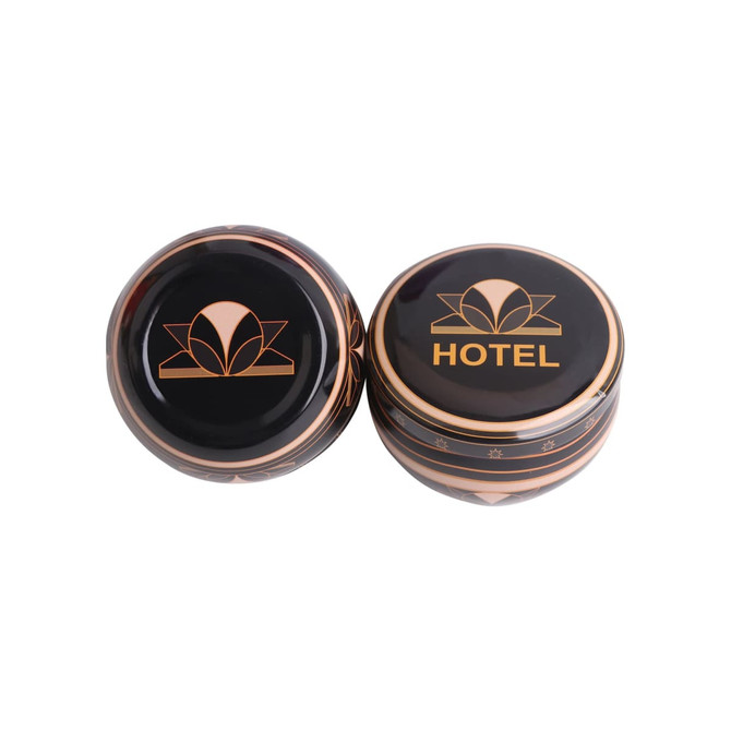 Two black tin candles with gold designs, one featuring a logo and the word "HOTEL". Two black tin candles with gold designs, one featuring a logo and the word "HOTEL".