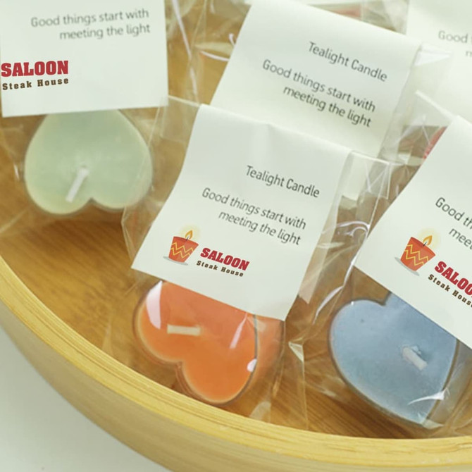 Tealight candles in various pastel colours, packaged in clear bags, arranged in a wooden bowl.