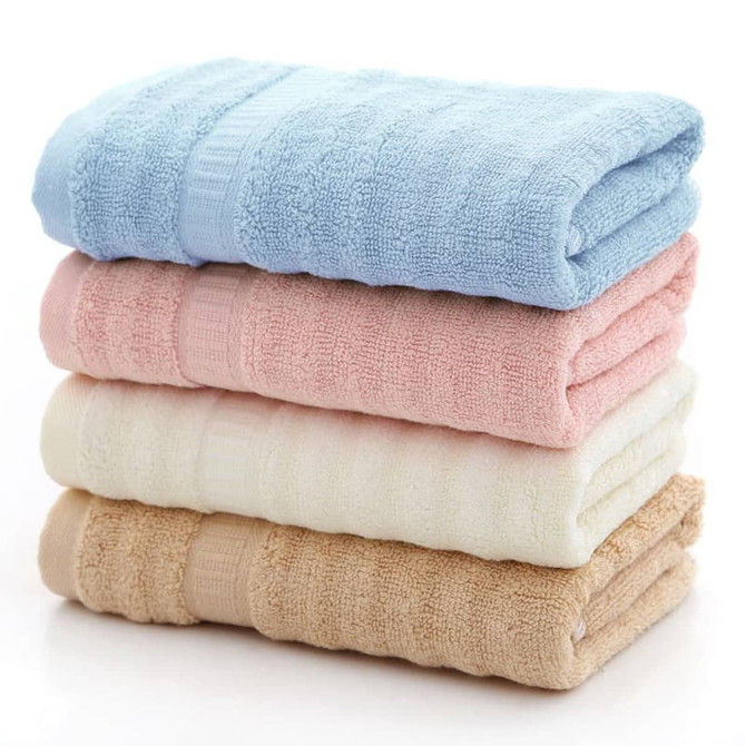A stack of bamboo fiber towels in blue, pink, cream, and beige, neatly folded with a textured design. A stack of bamboo fiber towels in blue, pink, cream, and beige, neatly folded with a textured design.