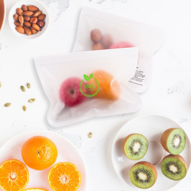 A large transparent storage bag filled with an apple, orange, and various nuts, surrounded by sliced kiwifruit and oranges.