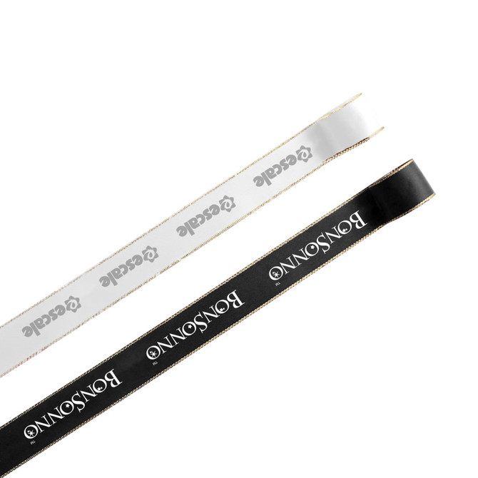 A length of ribbon in white and black, each with a gold edge and featuring a logo.