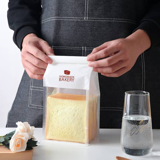 A transparent sealing storage bag holding a loaf of bread, featuring a logo and a white top closure. A transparent sealing storage bag holding a loaf of bread, featuring a logo and a white top closure.