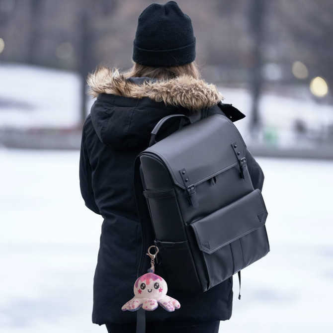 A black backpack features a small, reversible, octopus plush toy hanging from its side. The toy is pink and white.