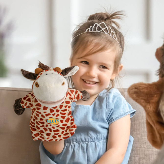 A plush giraffe hand puppet featuring brown and beige spots, held by a smiling child wearing a blue dress.