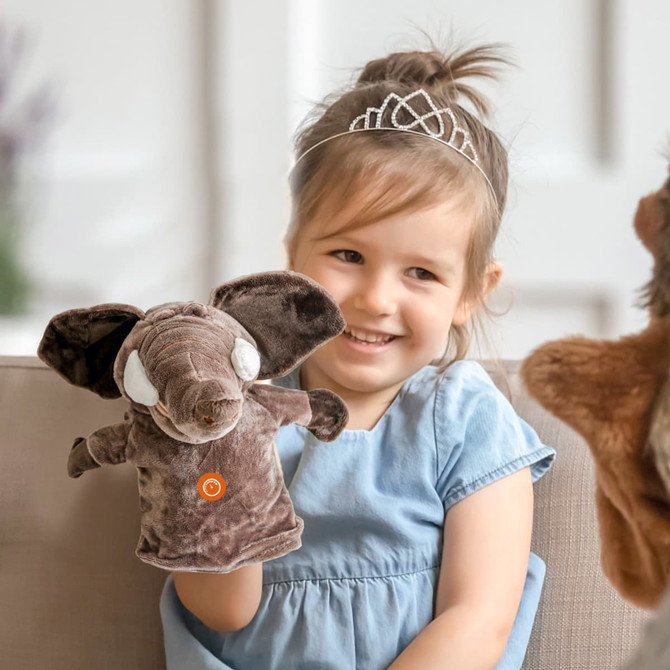 A plush elephant hand puppet in brown, held by a smiling child wearing a blue dress, with a tiara in her hair.