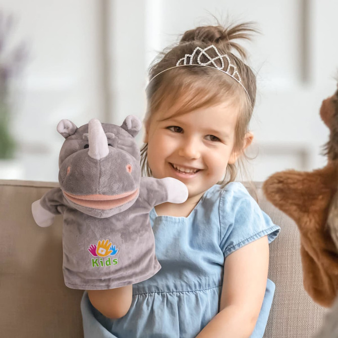 A grey plush rhino hand puppet with a smiling face, held by a child wearing a blue dress and a tiara.