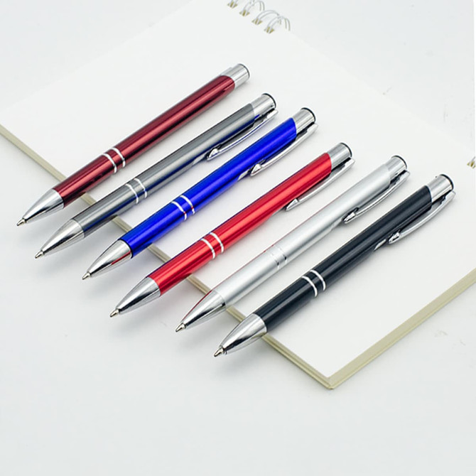 A collection of six metal click pens in red, blue, silver, black, and maroon, displayed with an open notepad.