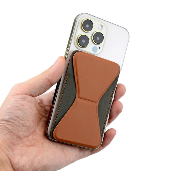 A hand holding a smartphone with a brown and grey PU MagSafe phone stand card holder attached to the back.