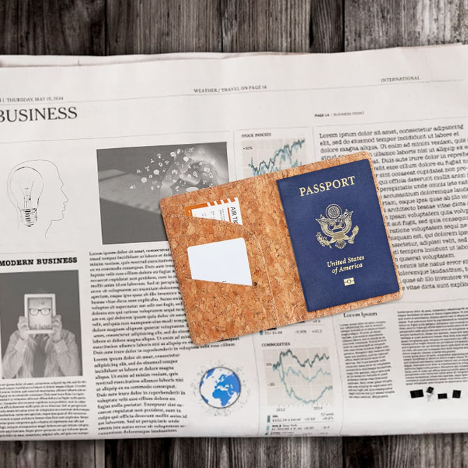 A cork passport holder in a tan colour with a blue passport inside, placed on a newspaper background.