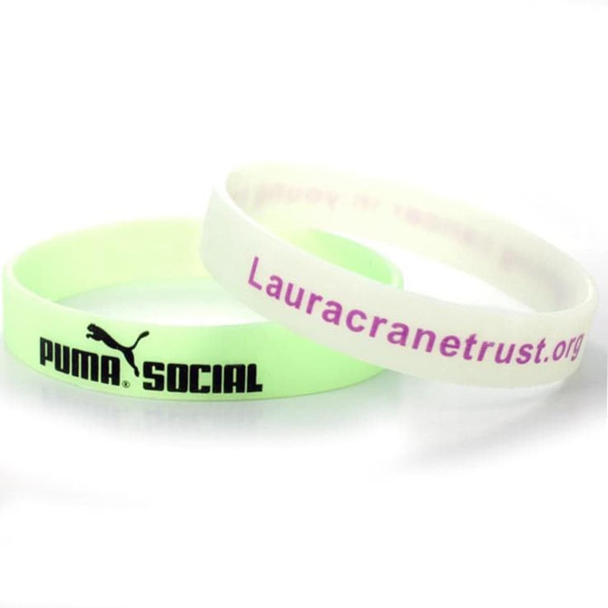 Two glow-in-the-dark silicone wristbands, one in pale green and the other white, featuring a logo on the green band. Two glow-in-the-dark silicone wristbands, one in pale green and the other white, featuring a logo on the green band.