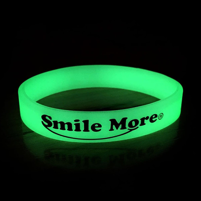 A green glow in the dark wristband with a logo, displayed against a dark background. A green glow in the dark wristband with a logo, displayed against a dark background.