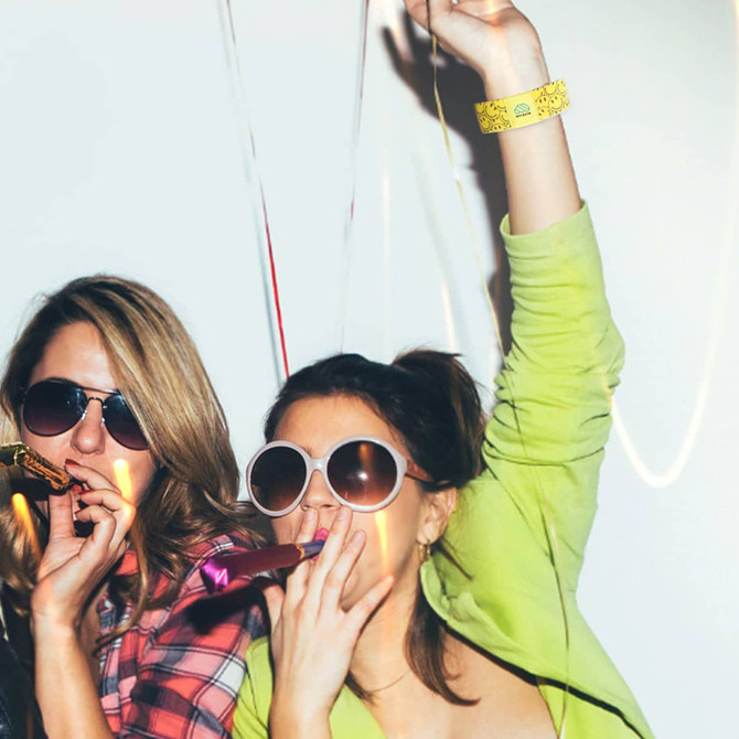 Two women wearing sunglasses, celebrating with party blowers and a yellow stretchy wristband on one wrist. Two women wearing sunglasses, celebrating with party blowers and a yellow stretchy wristband on one wrist.