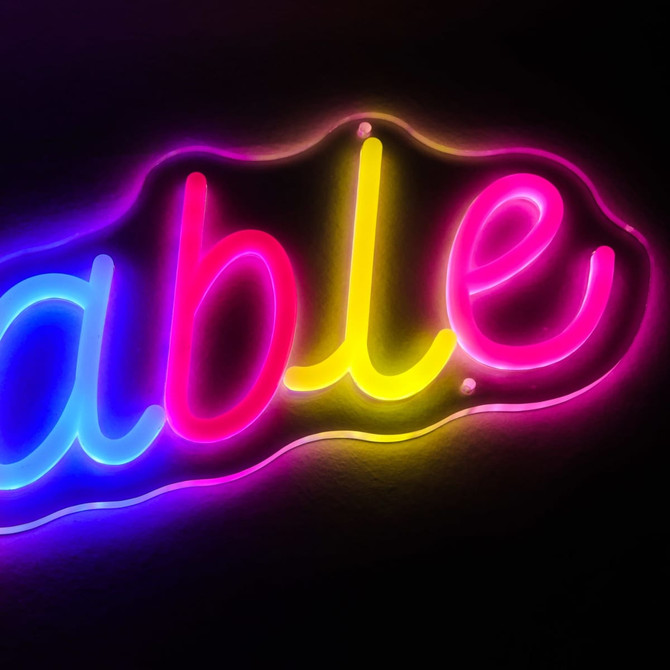 A neon LED sign in vibrant pink, yellow, and purple, featuring the word 'able' in a decorative font.