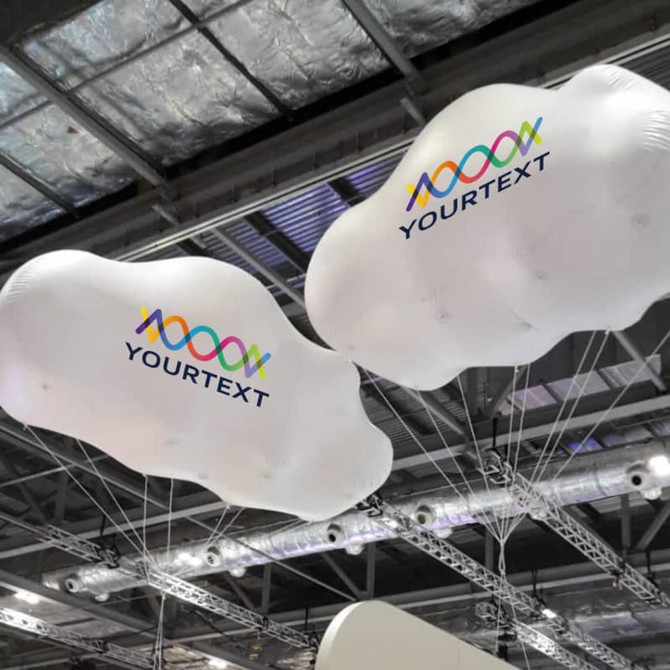 Two large white inflatable clouds with a logo, suspended from the ceiling at an exhibition event.