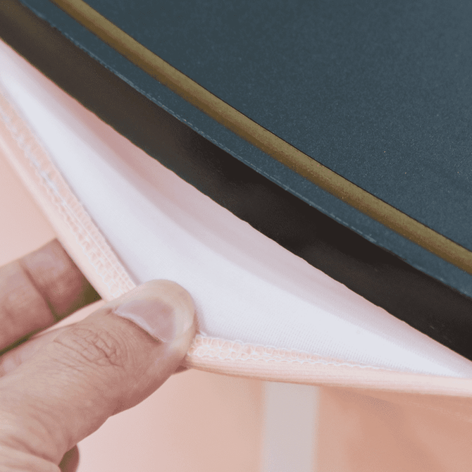 A close-up of a person's hand holding the edge of a triangular popup booth with peach fabric and a black backing. A close-up of a person's hand holding the edge of a triangular popup booth with peach fabric and a black backing.