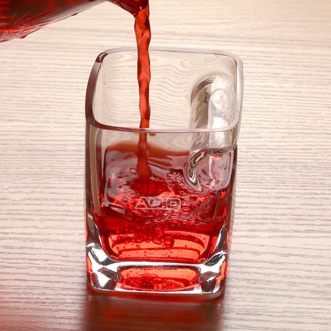 A square glass filled with a vibrant red liquid, with bubbles visible, placed on a wooden surface. The glass features a logo. A square glass filled with a vibrant red liquid, with bubbles visible, placed on a wooden surface. The glass features a logo.