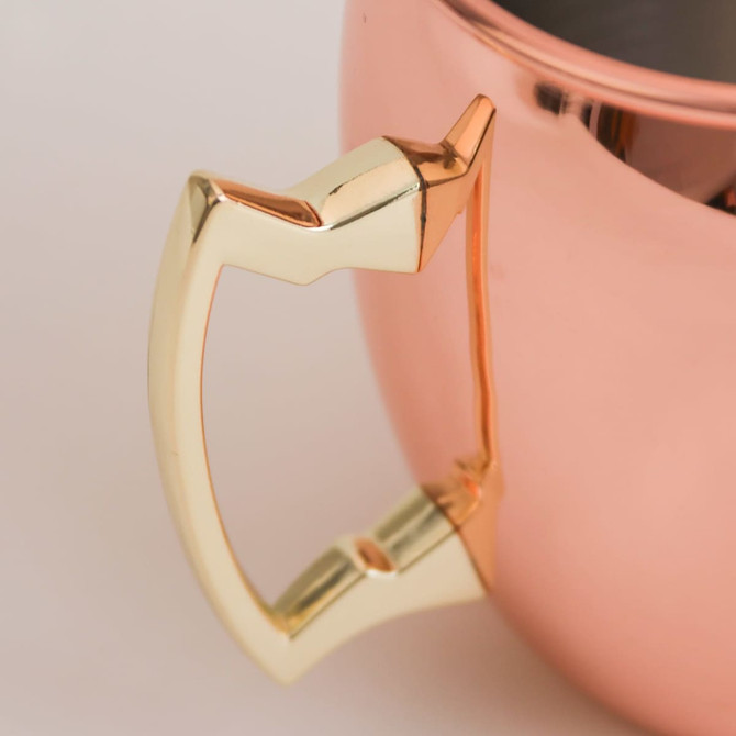 A copper mug with a gold-coloured handle, featuring a smooth, polished surface.