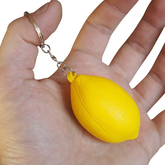 A yellow lemon-shaped stress reliever attached to a keyring, held in a hand. It has a shiny silver chain. A yellow lemon-shaped stress reliever attached to a keyring, held in a hand. It has a shiny silver chain.
