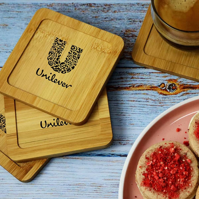 A set of bamboo coasters featuring a logo, placed on a wooden table alongside a drink and cookies.