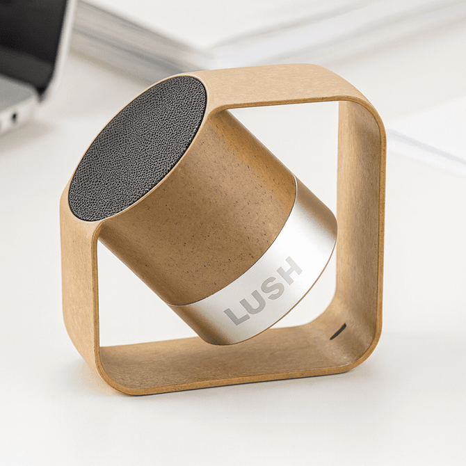 A wireless speaker featuring a plant fibre body and aluminium accents in natural tones, with a logo displayed prominently.