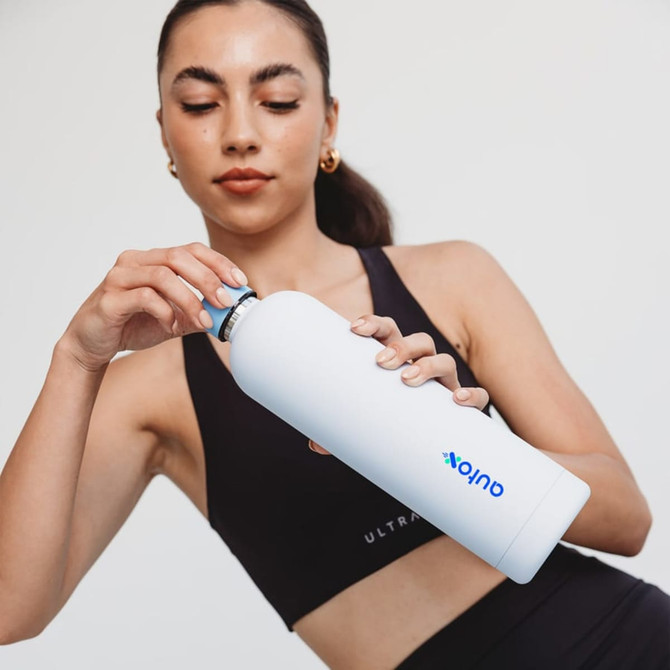 A drink bottle in white being held by a woman. The bottle features a logo and has a sleek design.