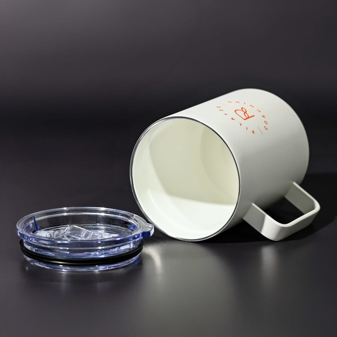 A travel mug in white with a handle and a transparent lid, positioned on a dark surface.