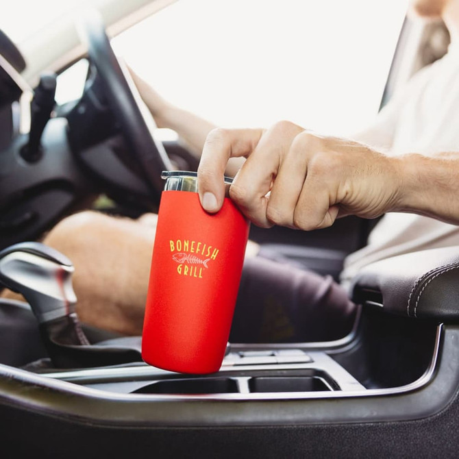 A drink bottle with a red exterior and a logo, placed in a car cup holder.
