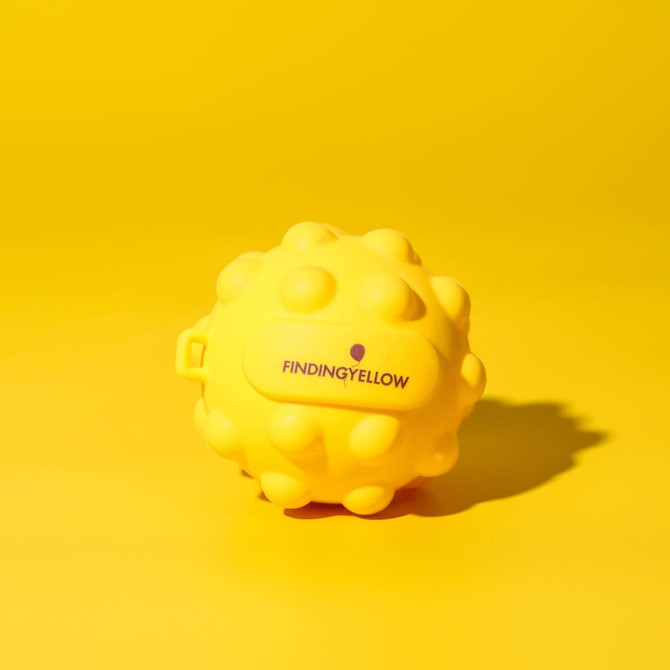 A yellow stress ball with a textured, spiky surface, featuring a small logo on it.