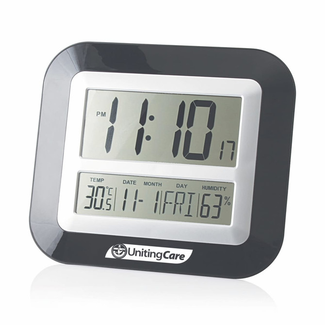 A wall desk clock with a black and silver design displaying time, temperature, date, day, and humidity. It features a logo.