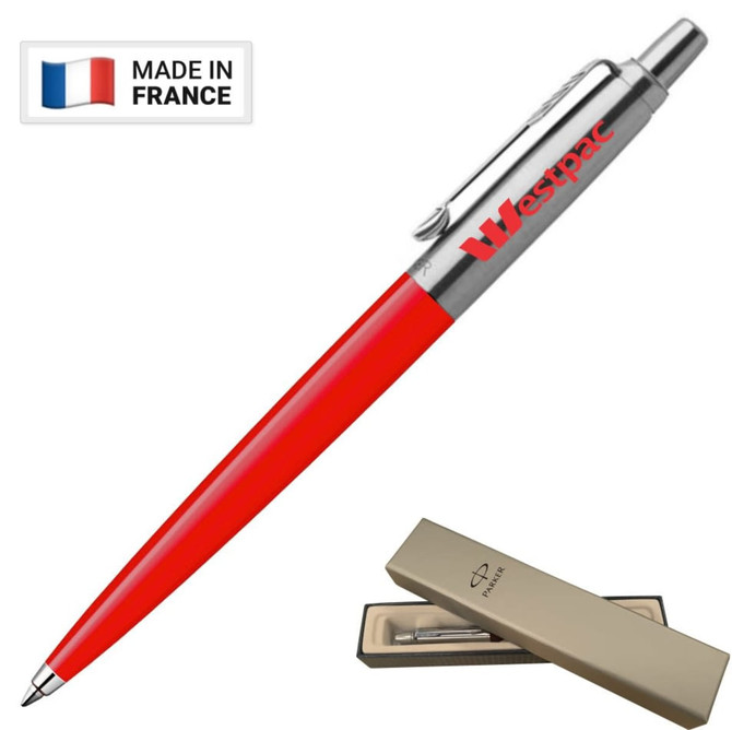 A metal ballpoint pen in red with a silver clip, presented in a beige box, featuring a brand logo.